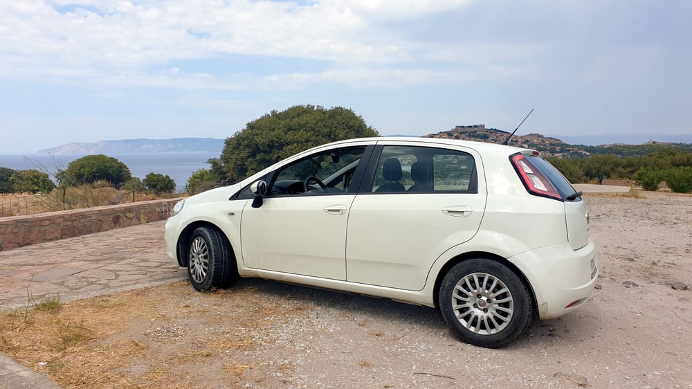 A white car parked with a view of the Lesbos coast.