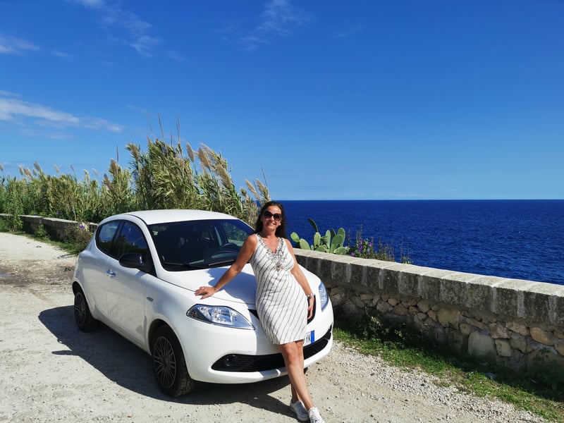 Woman in front of a white car on a coastal road in Italy