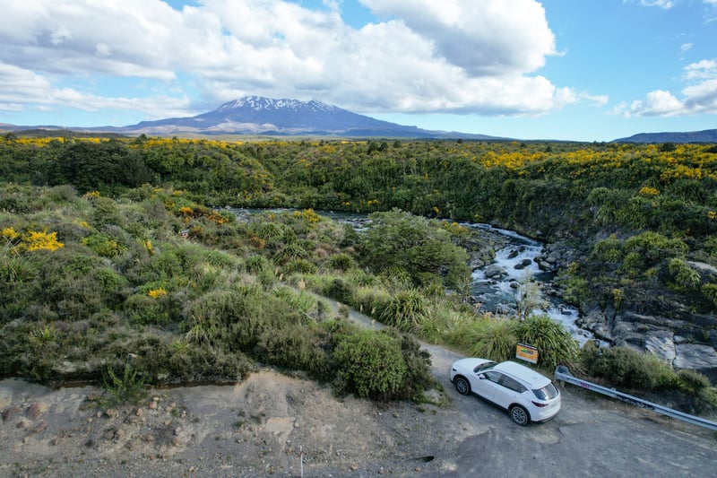 Viewing point over river, rocks and green mountains and a white car.