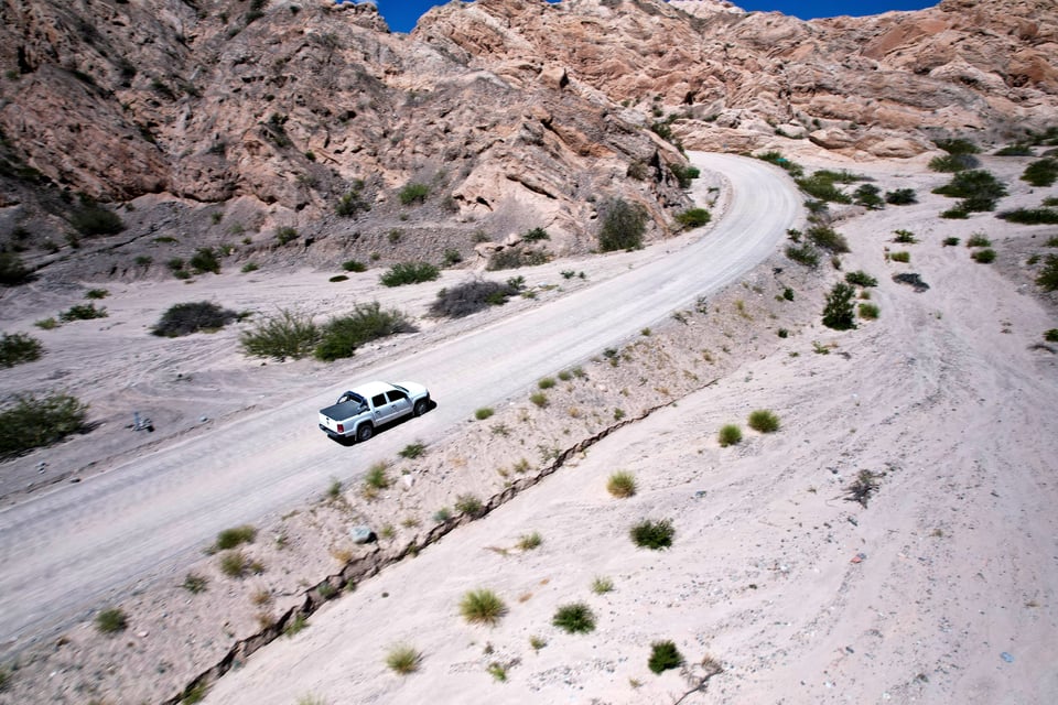 A white pickup truck on a gravel road winding between the rock walls of Quebrada de las Flechas, Argentina.